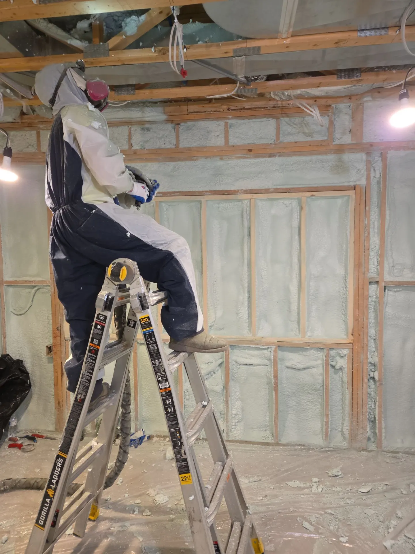 Foam-Tek technician on a ladder spraying foam insulation across basement walls